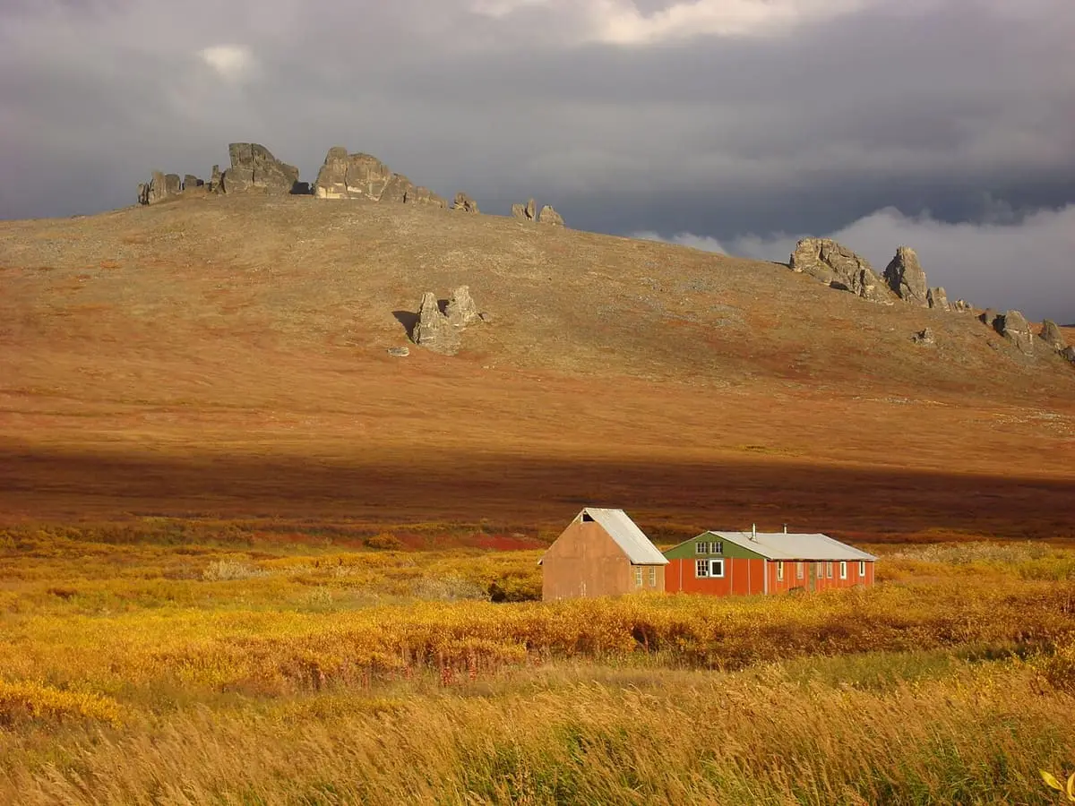 Red bunkhouse at Serpentine Hot Springs below granite tors in golden autumn tundra