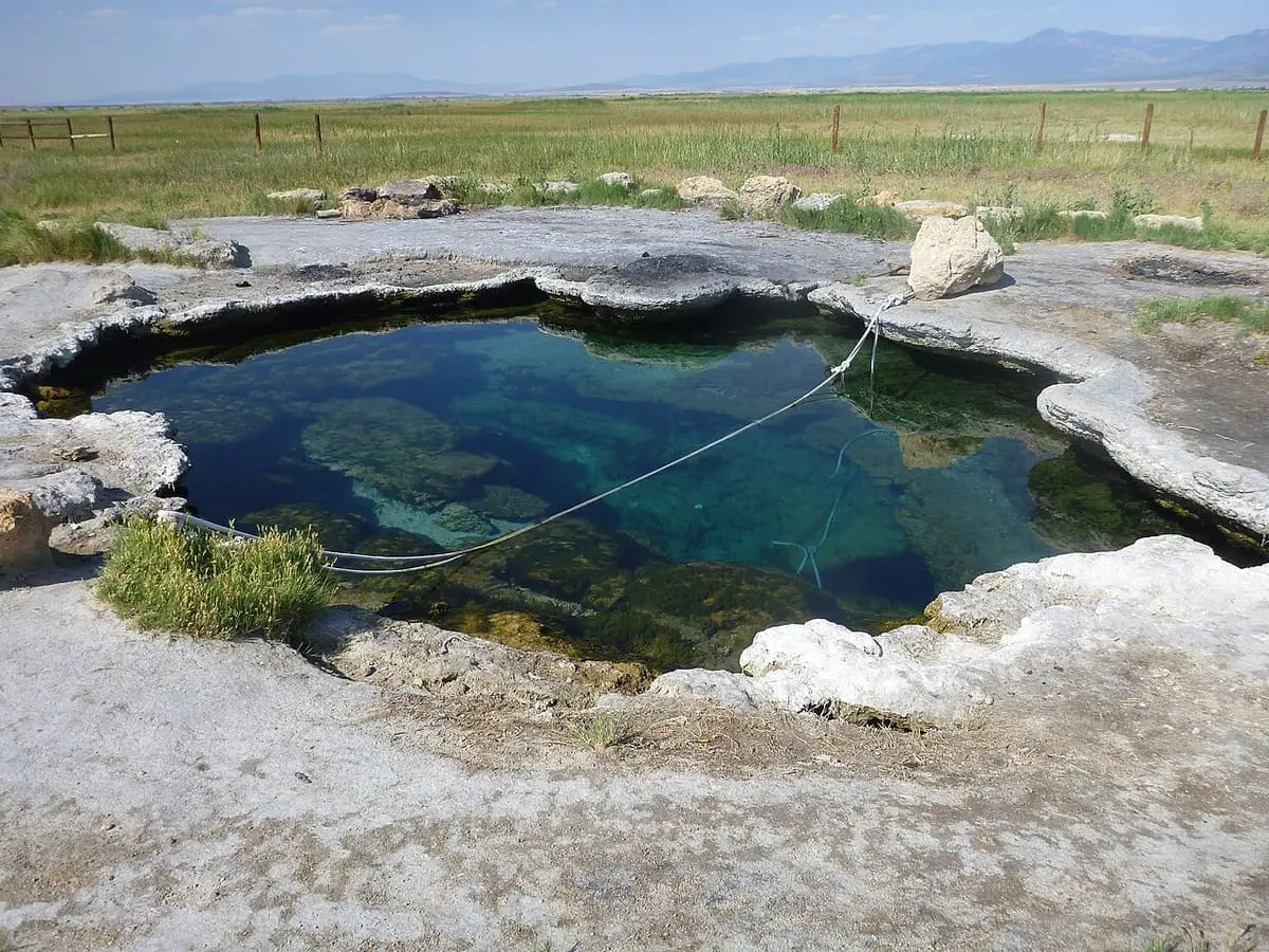 Deep blue green travertine soaking pool at Meadow Hot Springs with a rope across the water