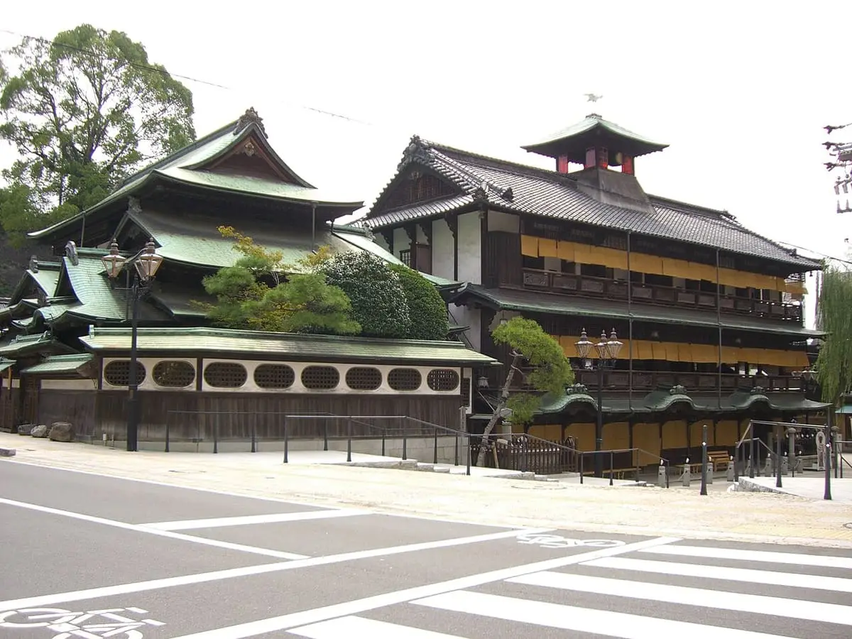 Dogo Onsen Honkan with layered tiled roofs and a small turret seen from the street corner