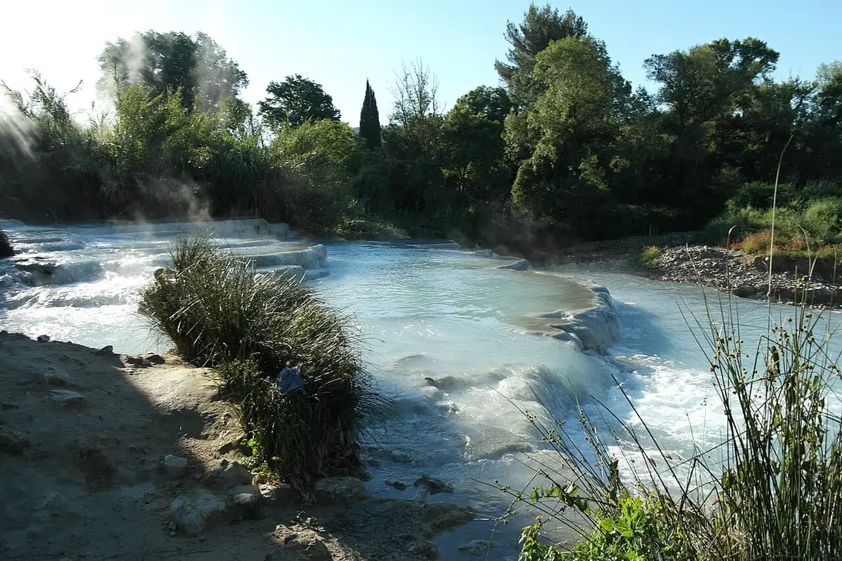 Milky blue thermal water spilling over travertine ledges among reeds at Cascate del Mulino