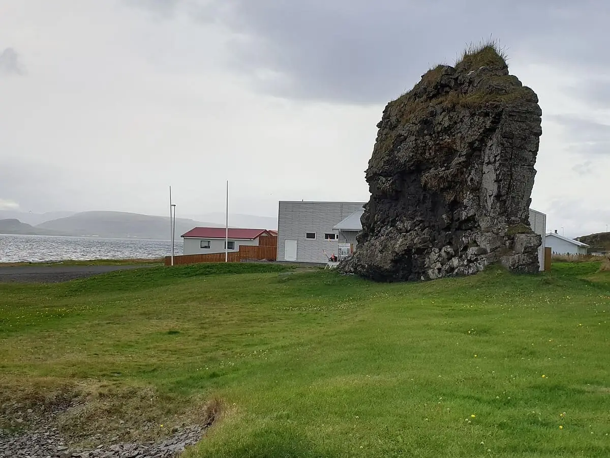 Kerling basalt rock pillar on a grassy lawn in Drangsnes village near the shore