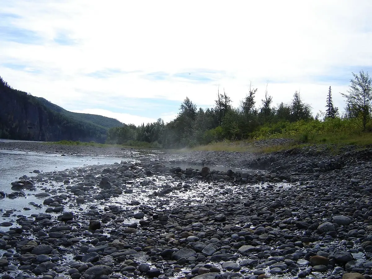 Rocky riverbank at Kraus Hotsprings along the South Nahanni River below forested cliffs