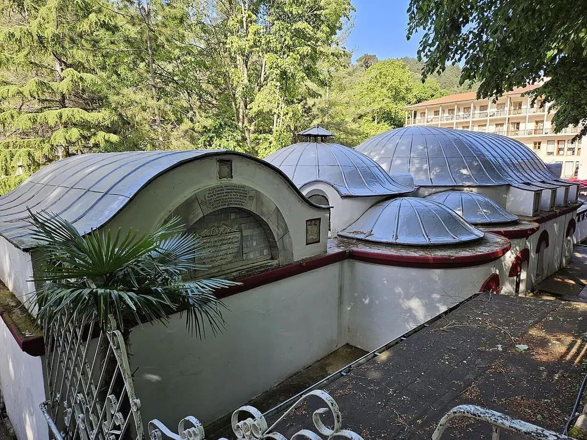 Lead domes of the historic Yalova Termal bathhouse surrounded by trees and a hotel