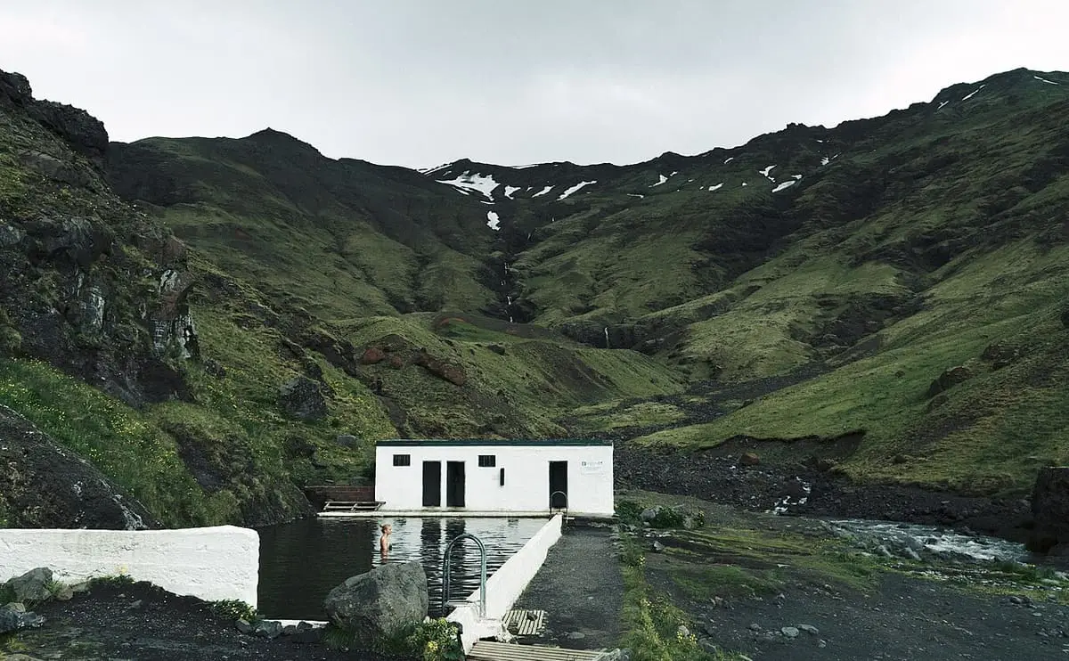 Seljavallalaug pool and changing house set below green mountain slopes with snow patches