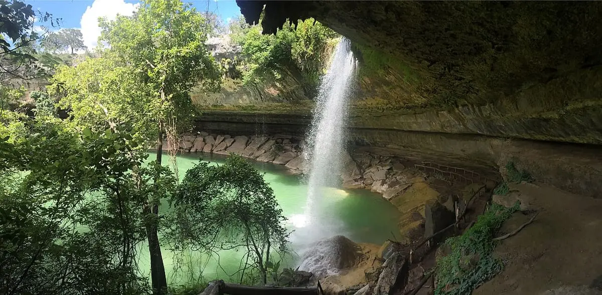 Hamilton Pool waterfall dropping into jade green water under a curved limestone ledge