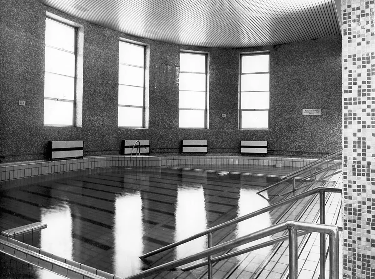Historic black and white view of an indoor pool with tall windows at Dandár Bath