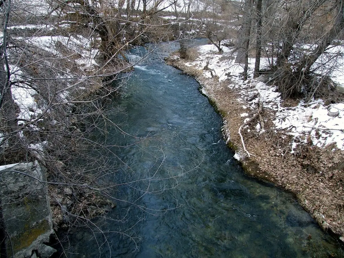 Clear Portneuf River running between snowy banks and bare trees in Lava Hot Springs
