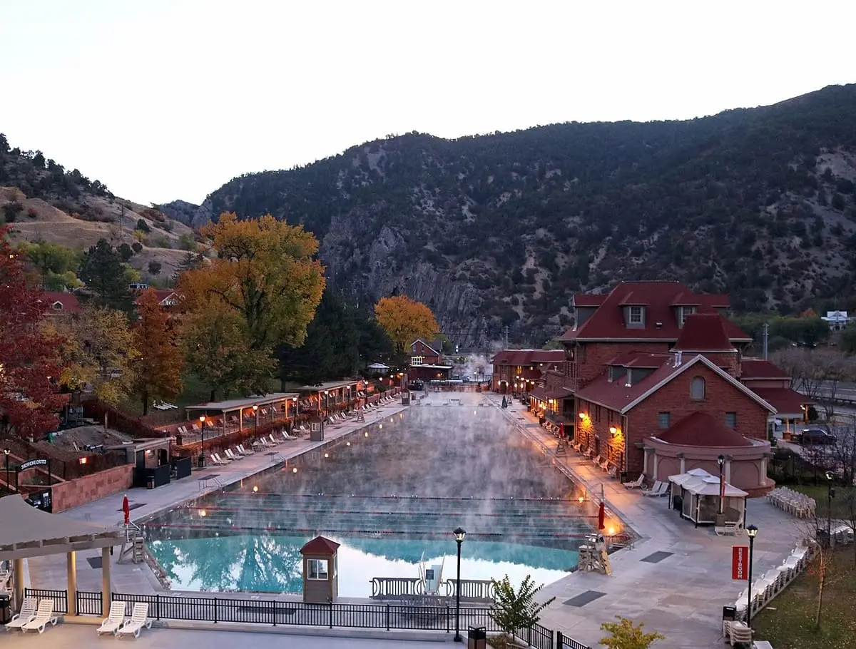 Steam rising off the long Glenwood Hot Springs Pool beside the red lodge among autumn trees