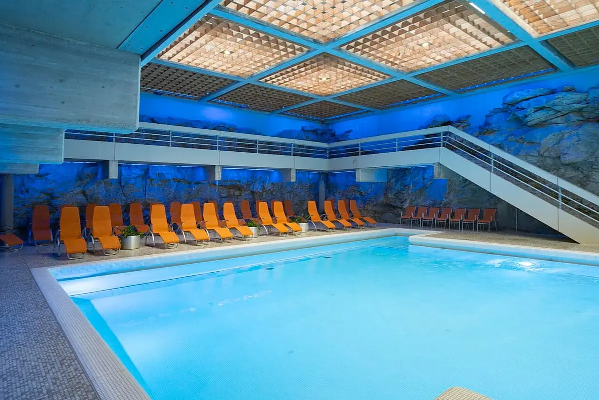 Indoor thermal pool at the Felsentherme with orange loungers and blue lit rock walls