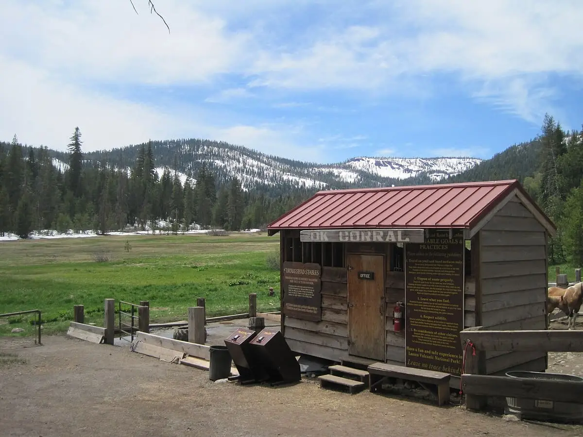 Weathered wooden corral building at Drakesbad Guest Ranch with a green Warner Valley meadow and snowy peaks