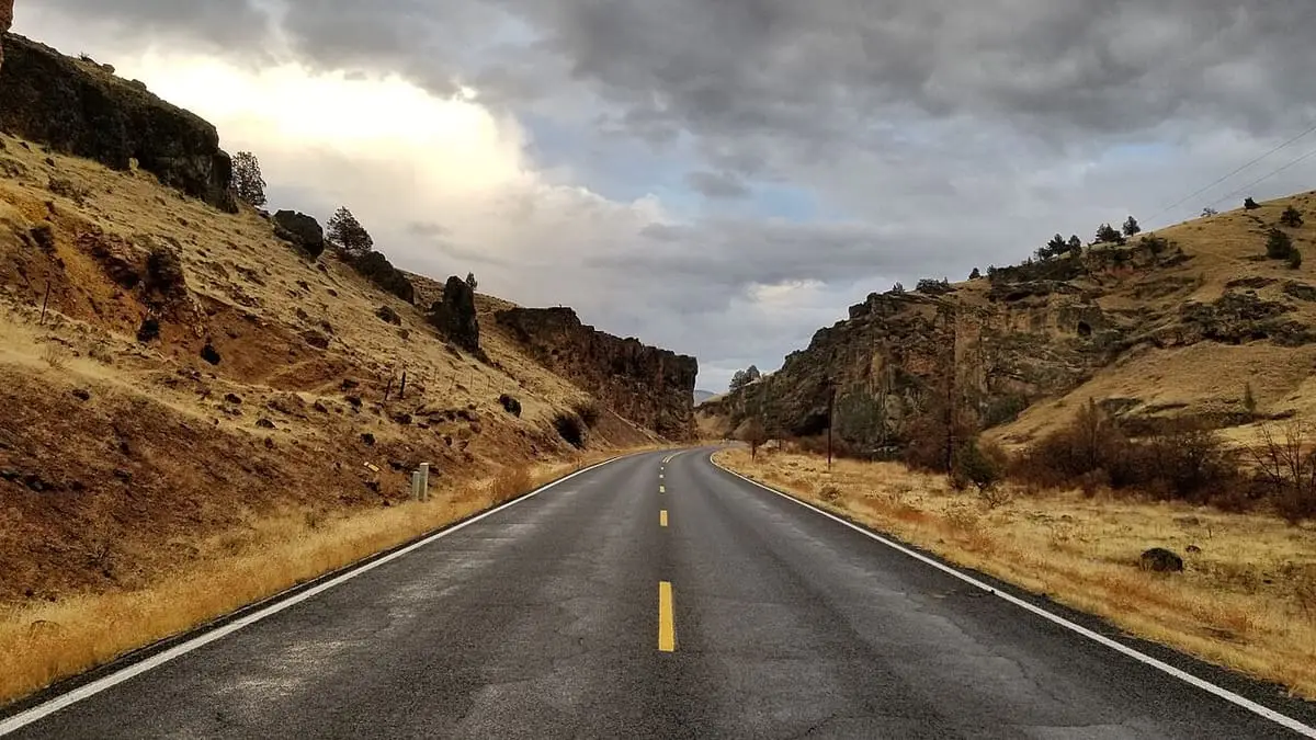Paved road winding through a rocky canyon toward Kah Nee Ta Resort under cloudy skies