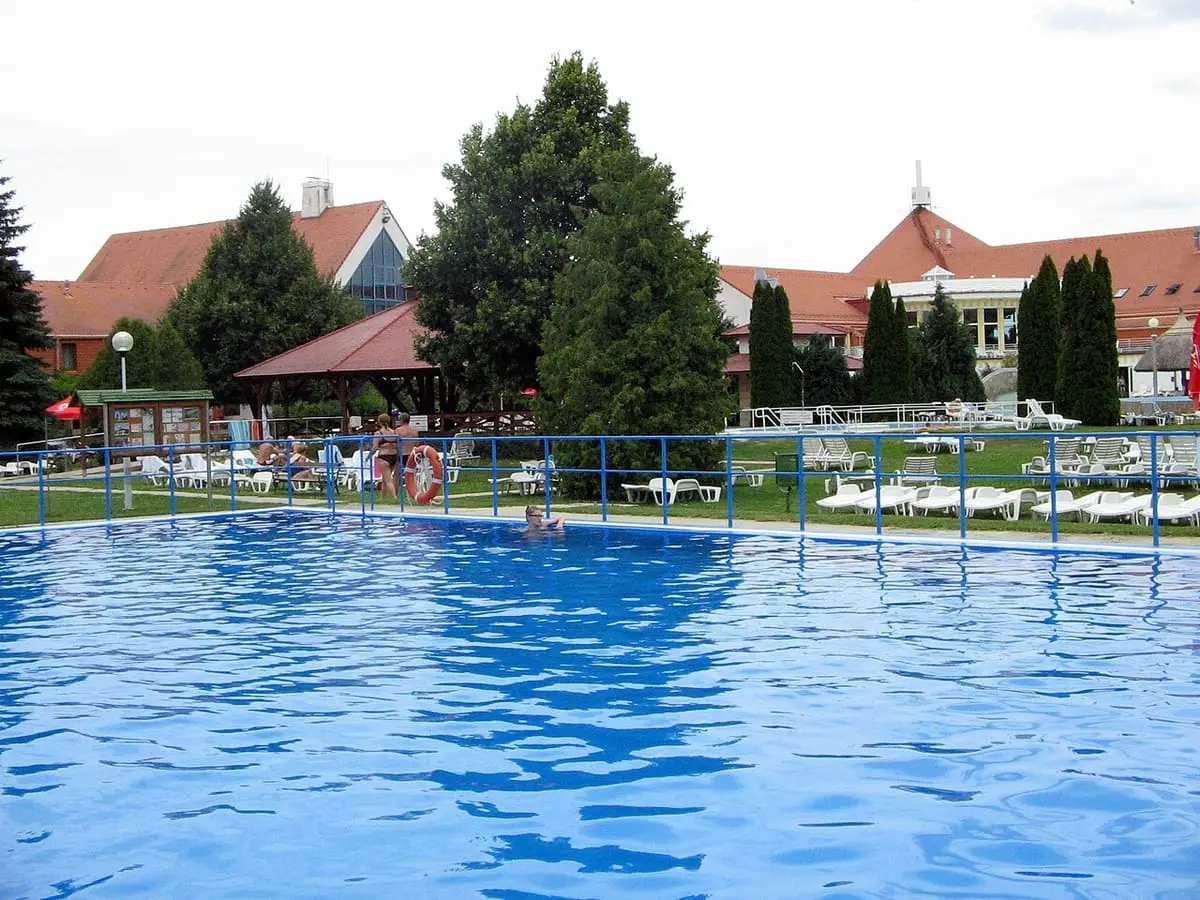 Large blue outdoor pool ringed by trees and loungers at Kehida Termál in Kehidakustány