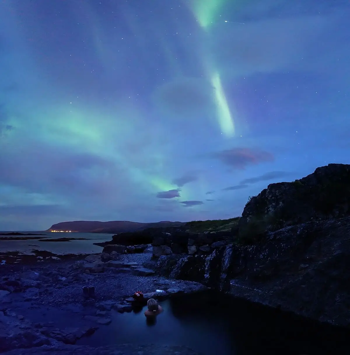 Green northern lights over the Hellulaug hot pot and the dark shoreline of Vatnsfjörður