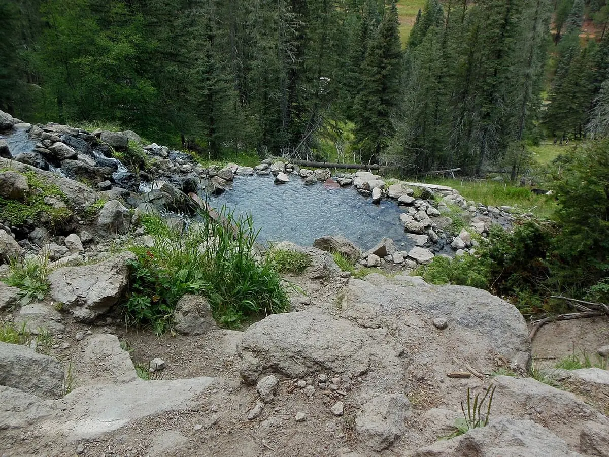 Blue grey soaking pool ringed with stones at San Antonio Hot Springs among spruce forest