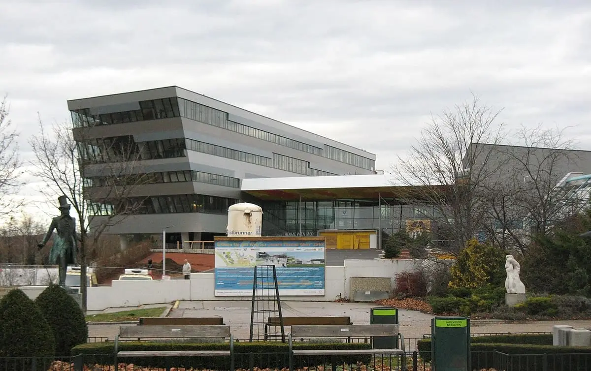Therme Wien building in Oberlaa seen across the forecourt with benches and a statue
