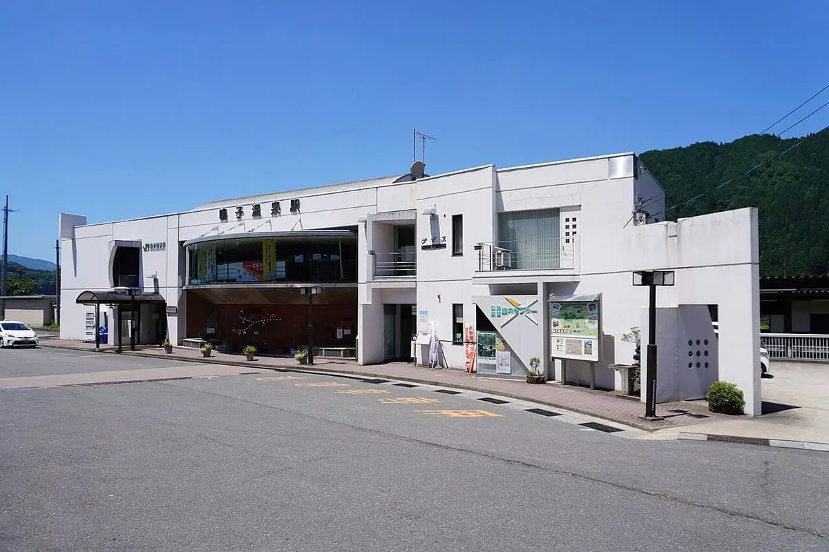 White Naruko Onsen station building on a sunny day with wooded hills behind