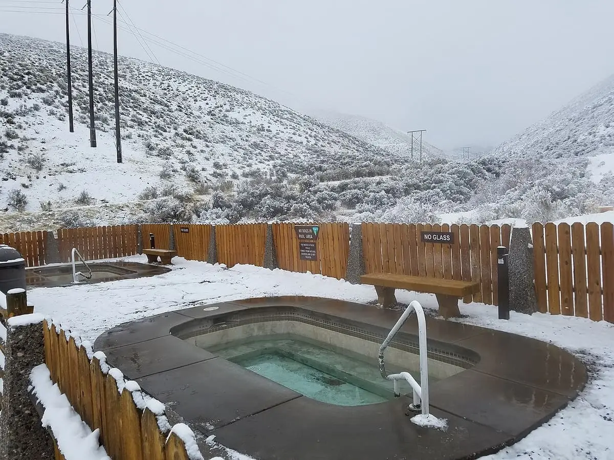 Concrete soaking pool with a handrail and wooden fence surrounded by snowy hills at Sharkey Hot Springs