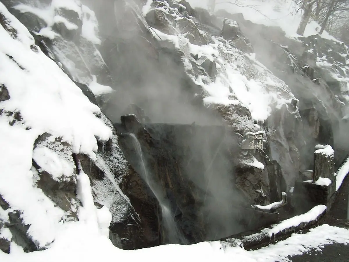 Steaming hot water falling over snowy rocks at Yunotaki in Jozankei Onsen