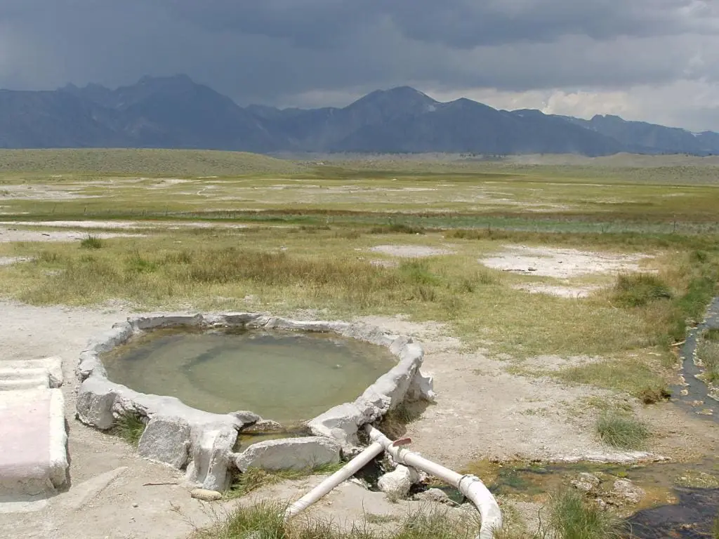 Hilltop Hot Springs tub on the open Long Valley flats under storm clouds with distant mountains