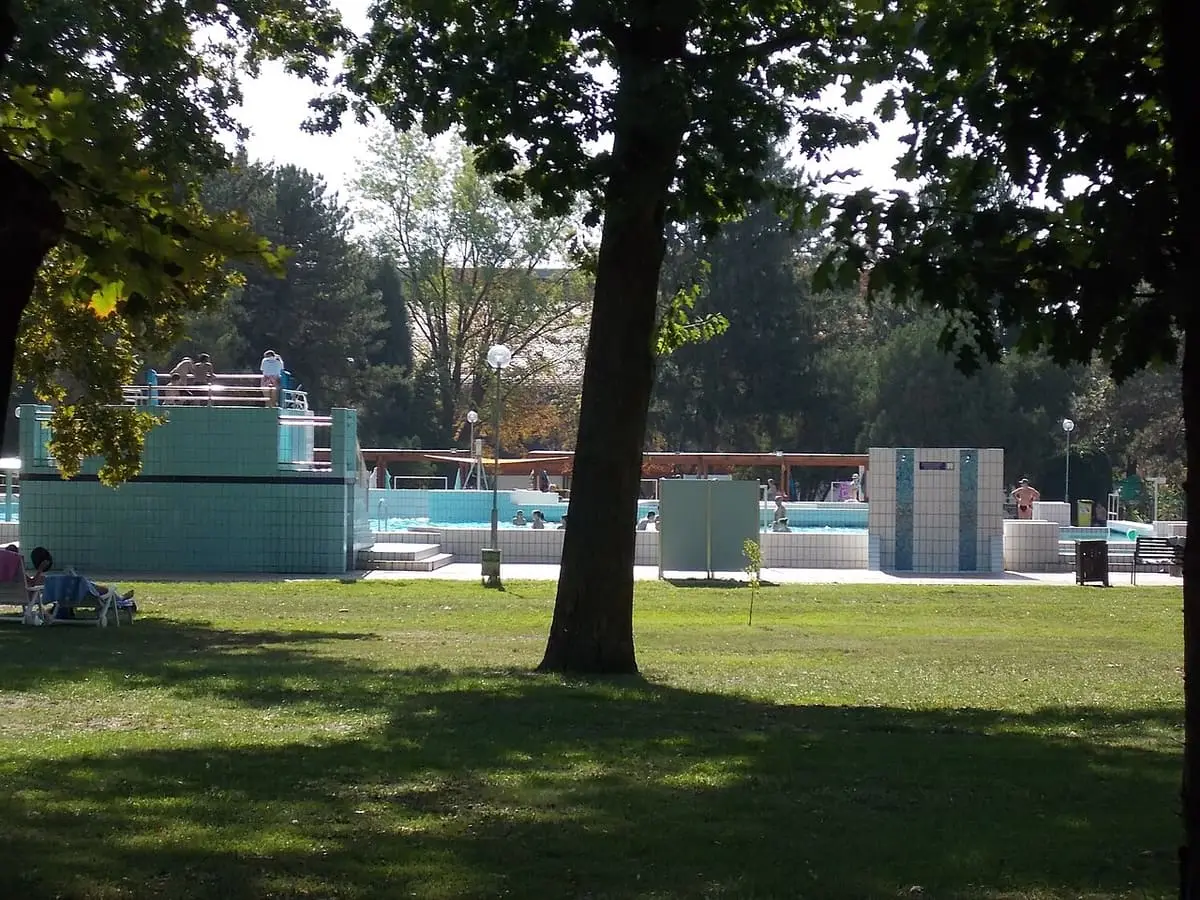 Tiled outdoor pools of the Zsóry bath seen past shade trees in Mezőkövesd
