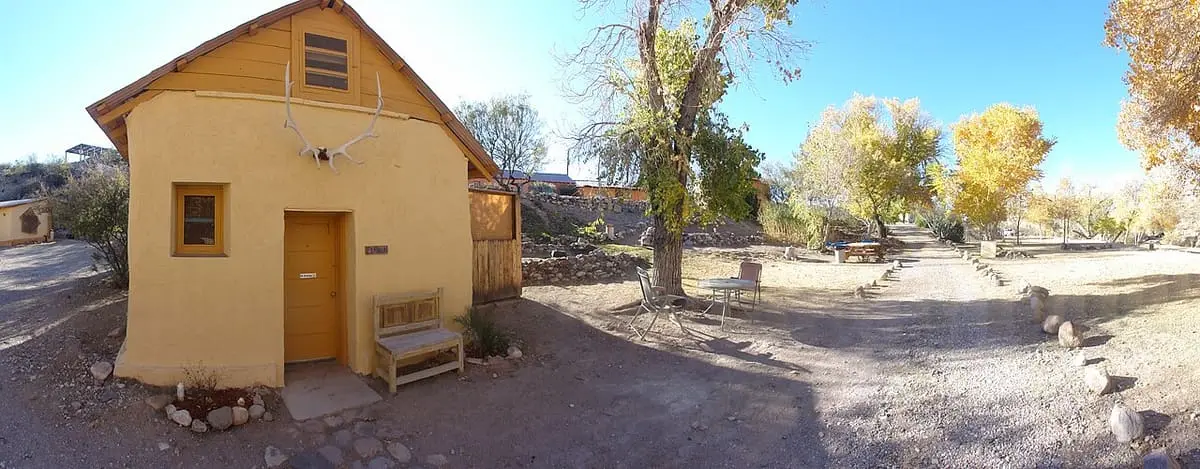 Yellow adobe El Patron cabin and gravel grounds under cottonwoods at Chinati Hot Springs