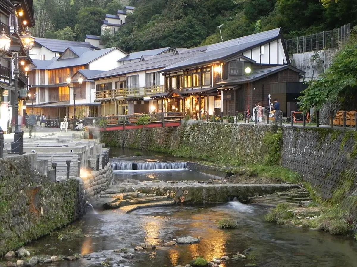 Ginzan Onsen inns along the stone banked river at dusk with lamps lit