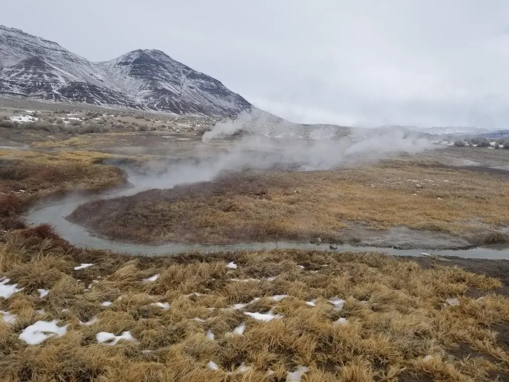 Winter steam drifting over a hot runoff channel at Mickey Hot Springs below snowy peaks