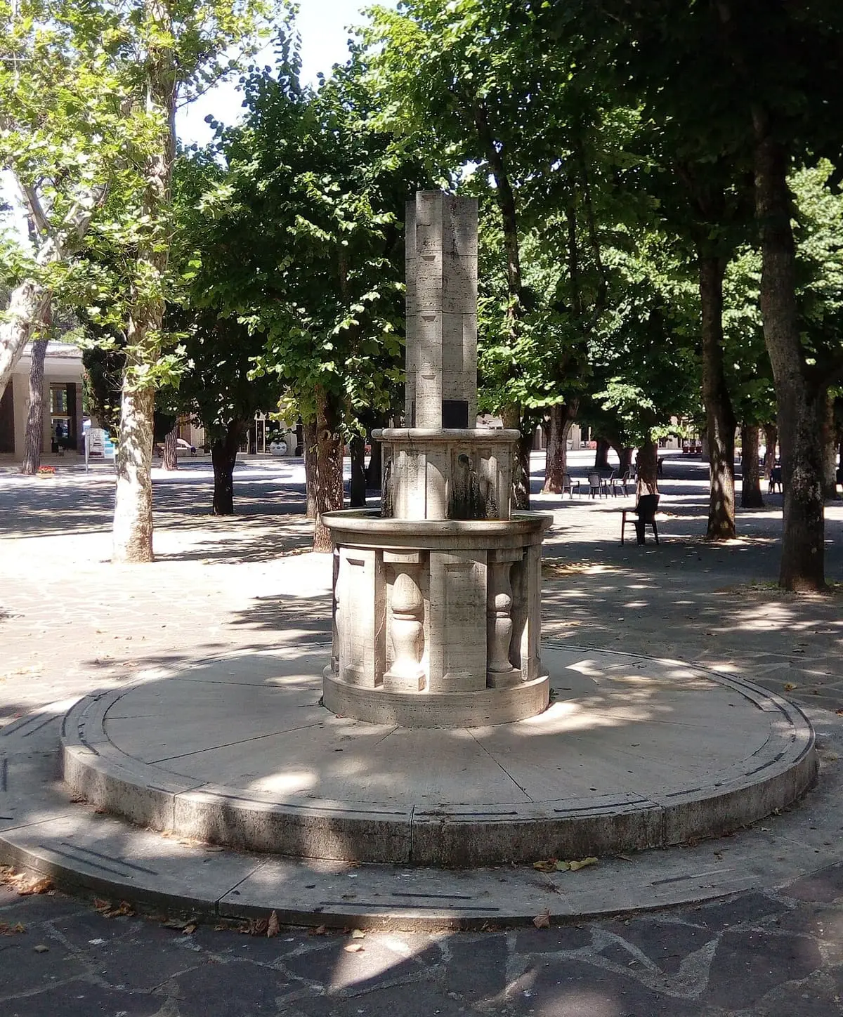Stone fountain under tall trees in the Acqua Santa spa park at Chianciano Terme