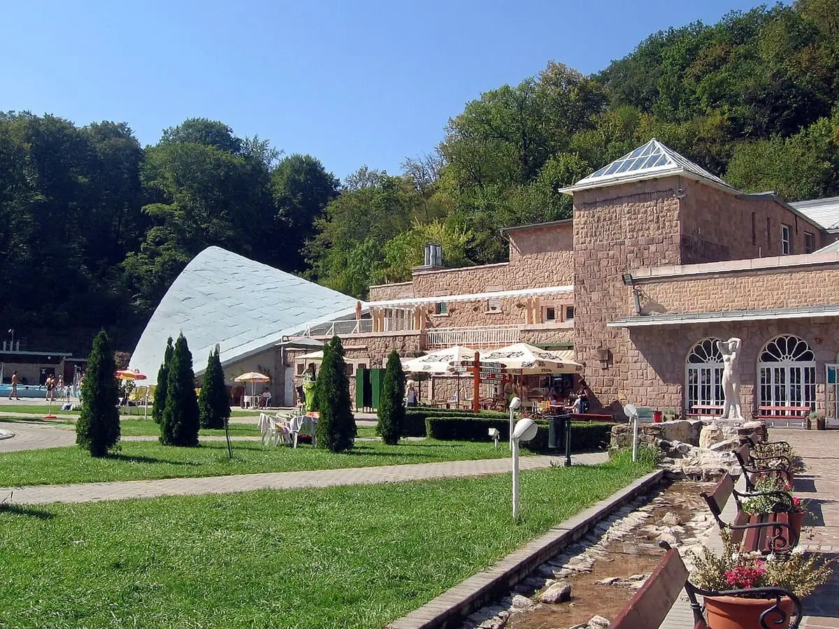 Brick bath building and white shell shaped roof among wooded hills at Miskolctapolca