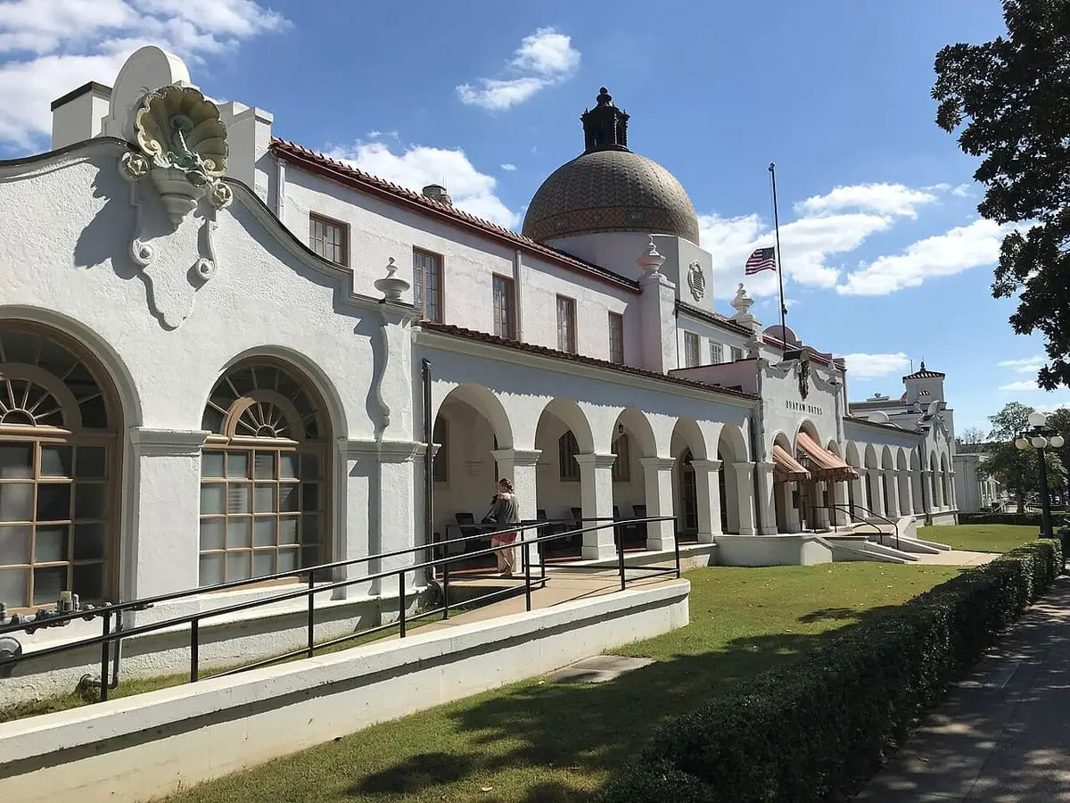 White arcaded facade and tiled dome of the Quapaw Bathhouse along a lawn under blue sky