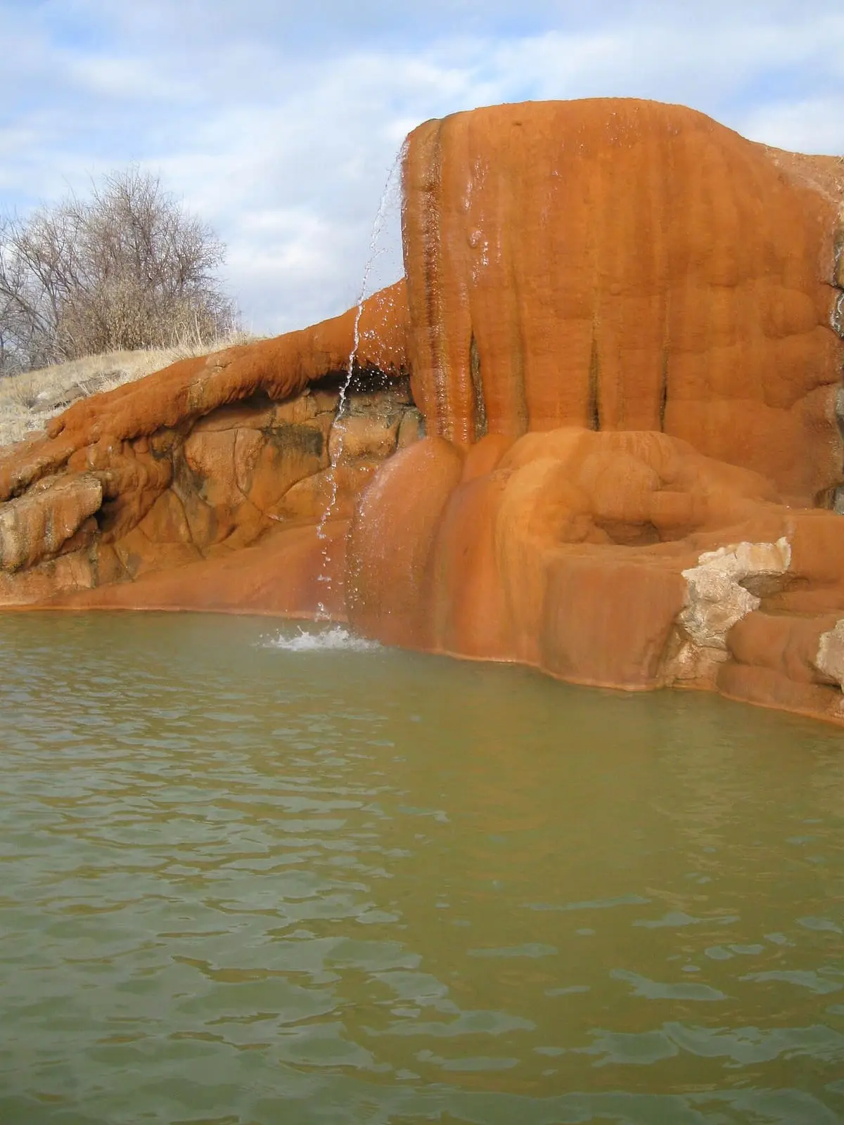 Hot water spilling from an orange travertine mound into a soaking pool at Mystic Hot Springs