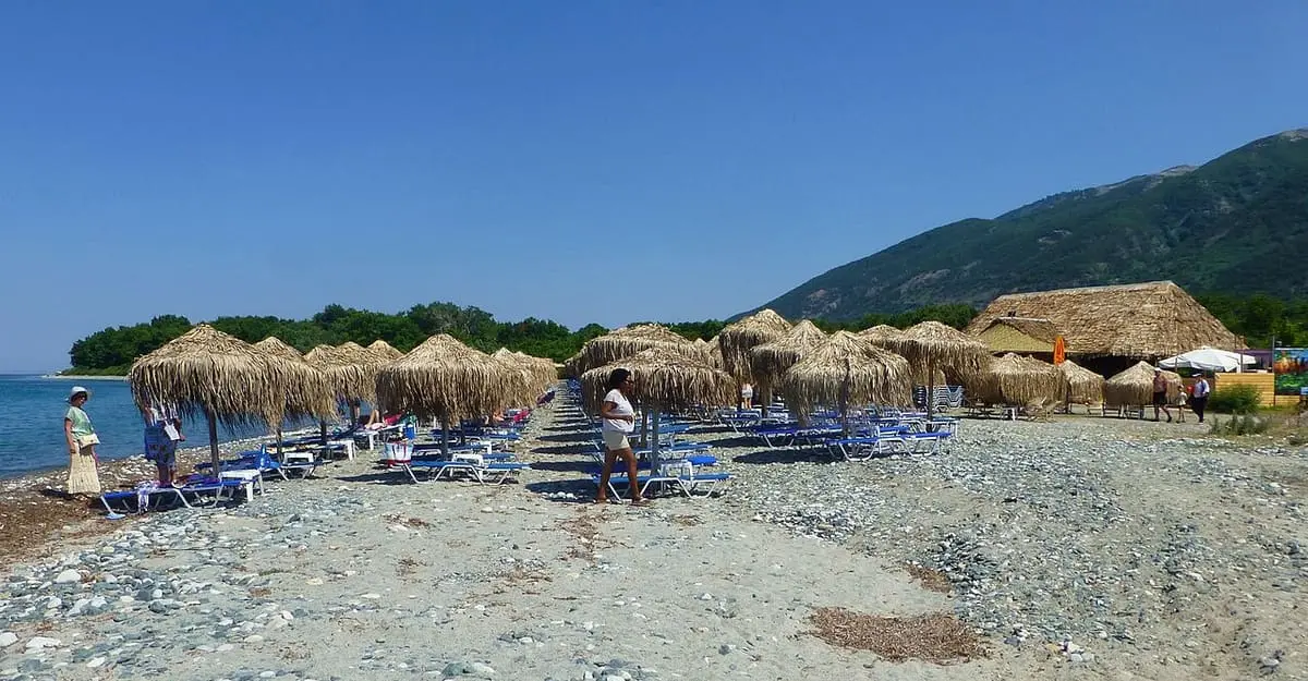 Thatched umbrellas and sunbeds on the pebble beach at Therma below the mountains of Samothraki