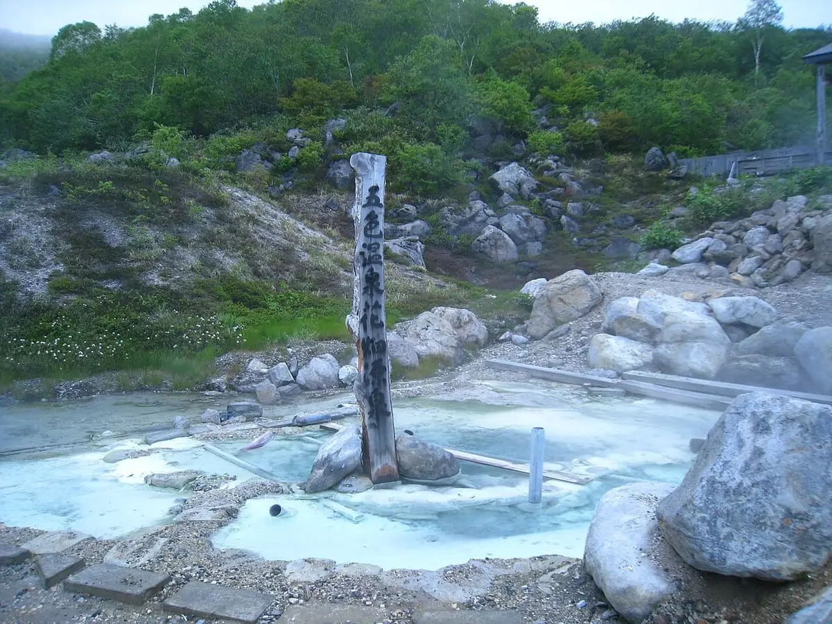 Milky hot spring source pool with a wooden post among rocks at Goshiki Onsen
