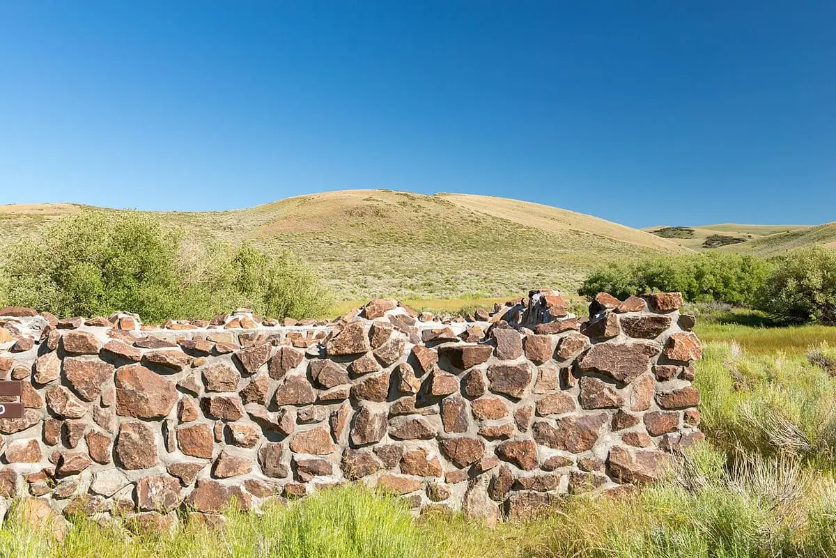 Rock wall of the Hart Mountain hot springs pool among green sagebrush under a clear blue sky