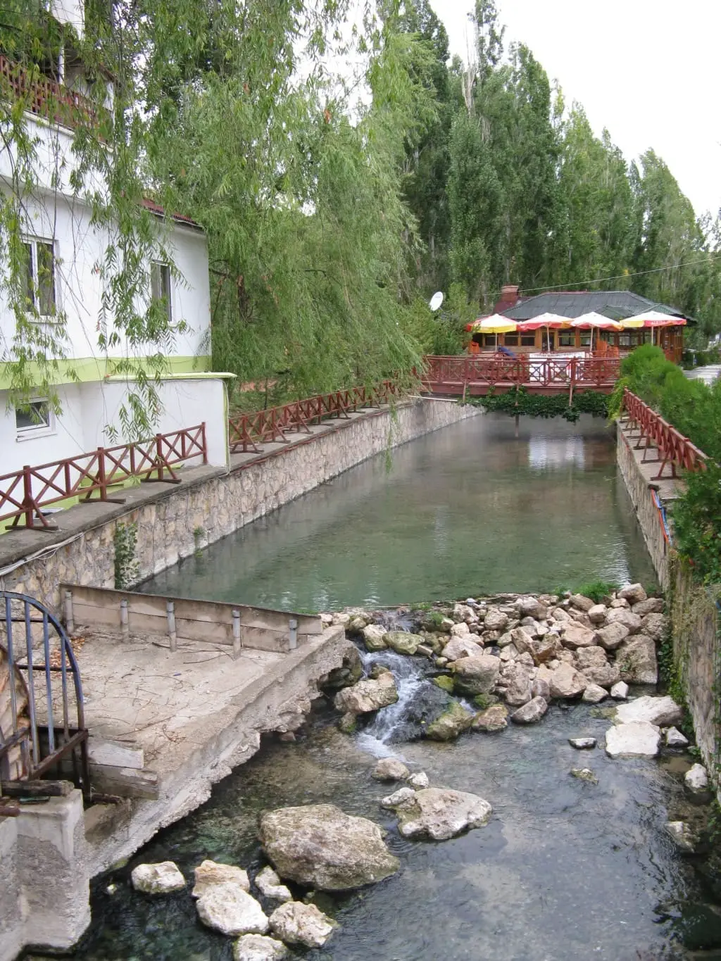 Stone walled thermal channel and rocks at Balıklı Kaplıca, Kangal, beside white buildings
