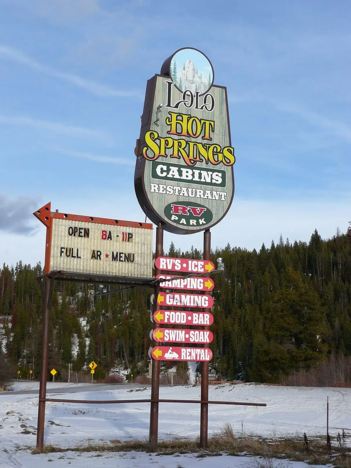 Tall roadside sign for Lolo Hot Springs cabins and restaurant against a blue winter sky