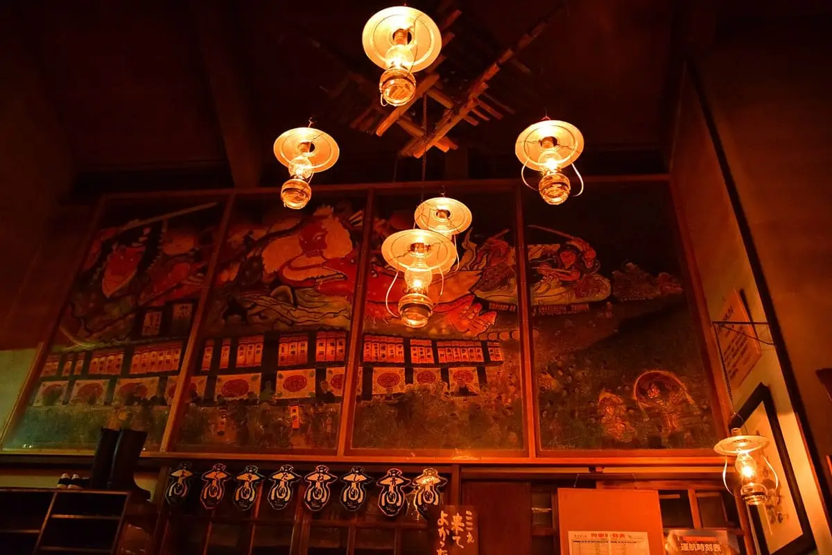 Glowing oil lamps hanging from the ceiling in front of painted panels at Lamp no Yado Aoni Onsen