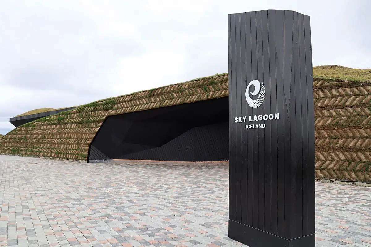 Sky Lagoon entrance with a black sign beside a curved turf wall
