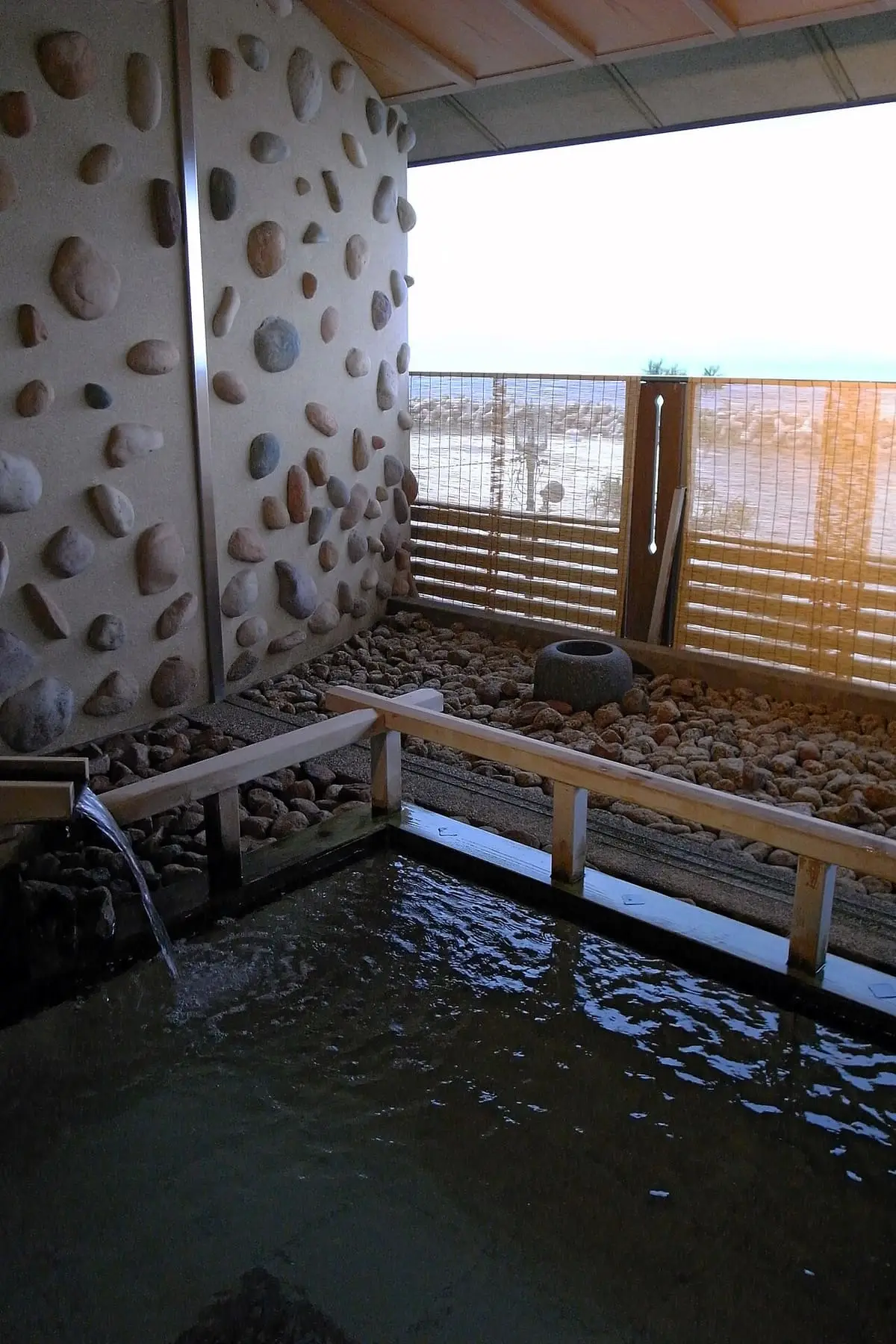Open air hot spring bath at Kaike Onsen with a stone wall and water spout facing the sea