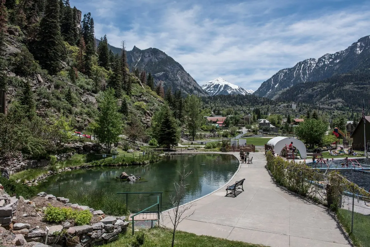 Landscaped pond and walkway at Ouray Hot Springs with snowy San Juan peaks beyond