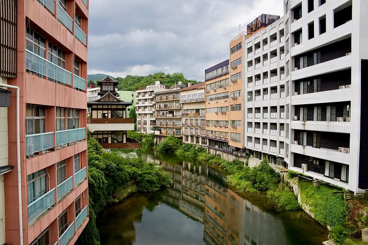 Hotel buildings and a traditional tower lining the green Surikami River at Iizaka Onsen