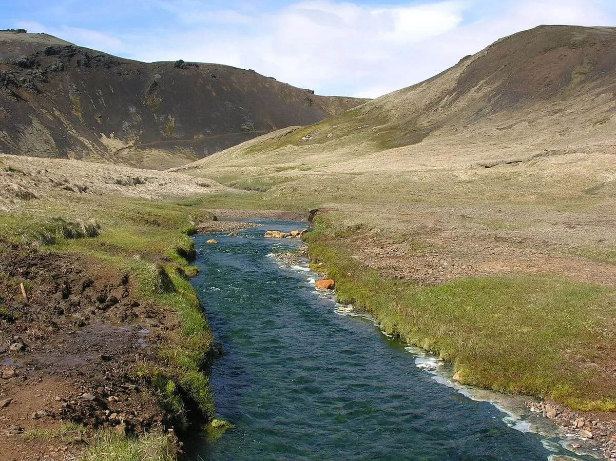 Reykjadalur thermal river flowing between grassy banks below bare brown hills