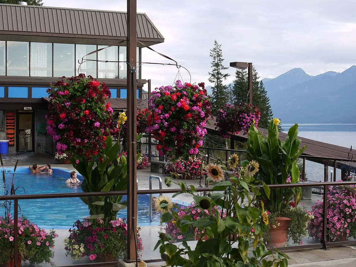 Hot pool framed by hanging flower baskets with Kootenay Lake and mountains in the distance