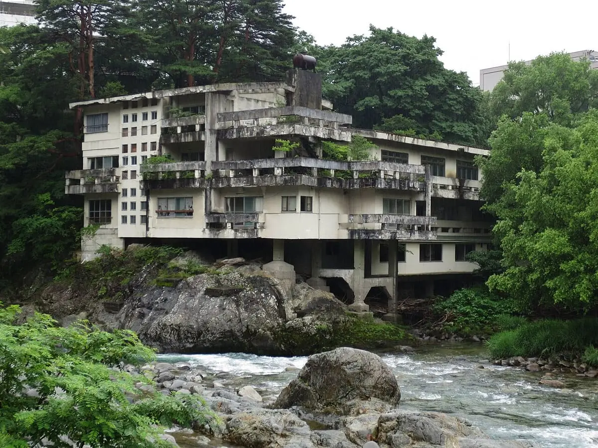 Sokai Hotel above a rocky river with forest behind at Minakami Onsen