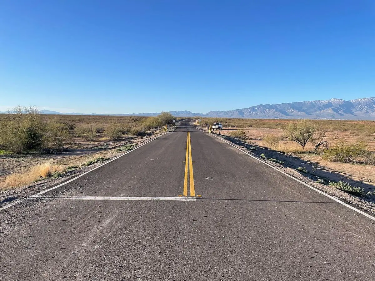 Paved Haekel Road crossing open desert toward Hot Well Dunes Recreation Area with mountains ahead