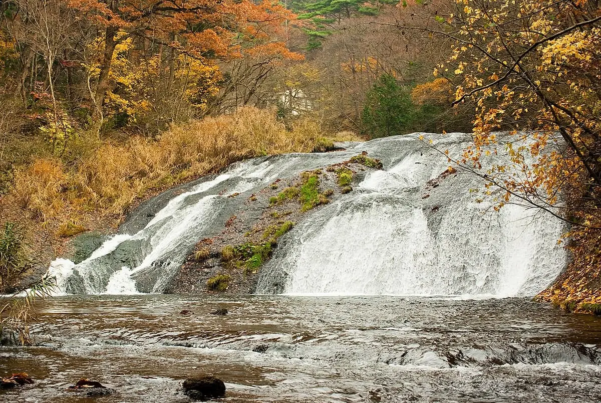 Kamabuchi Falls spilling over broad rock ledges among autumn trees near Hanamaki Onsen