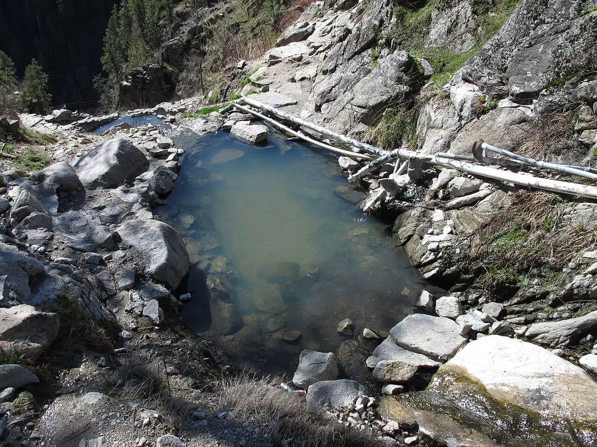 Murky user built rock pool with pipes on a rocky slope at Skinny Dipper Hot Springs