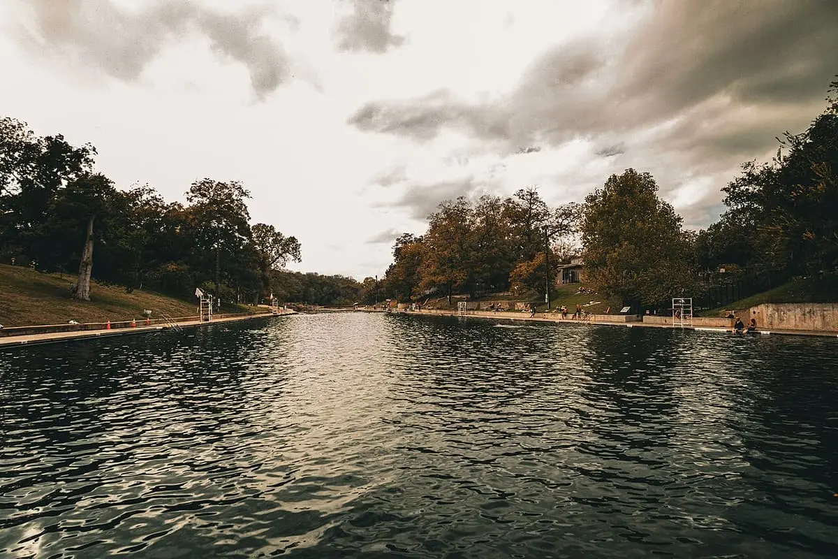 Long view down Barton Springs Pool under dramatic clouds with trees lining both banks