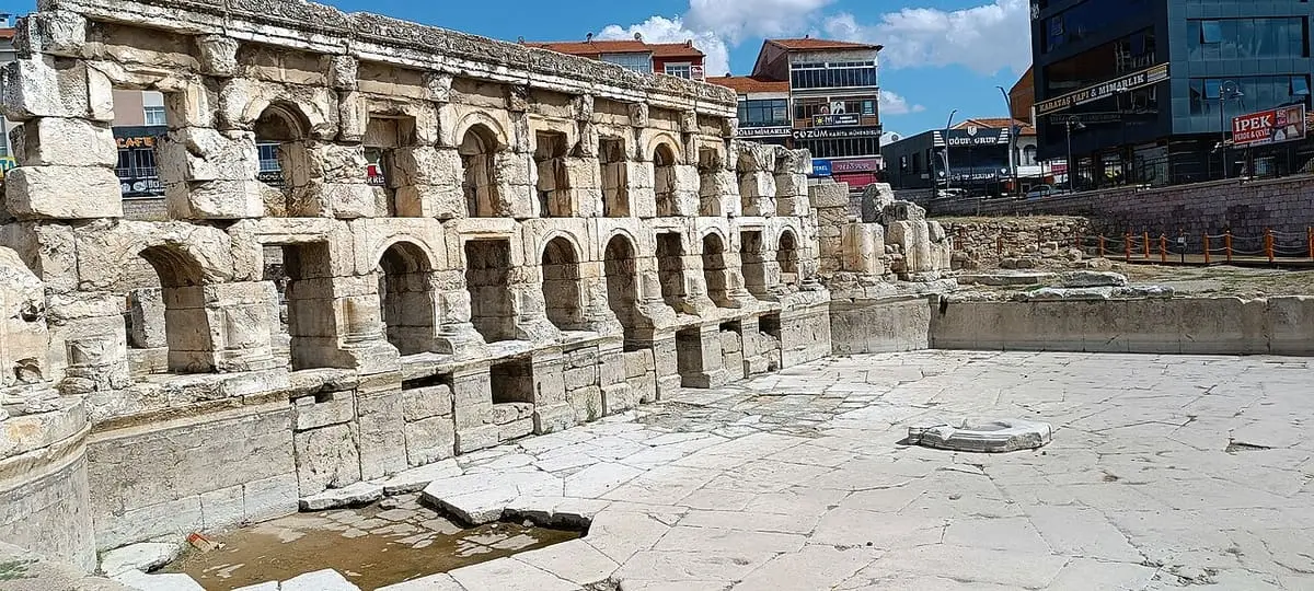 Close view of the arched niches along the Sarıkaya Roman Bath wall with water on the paving