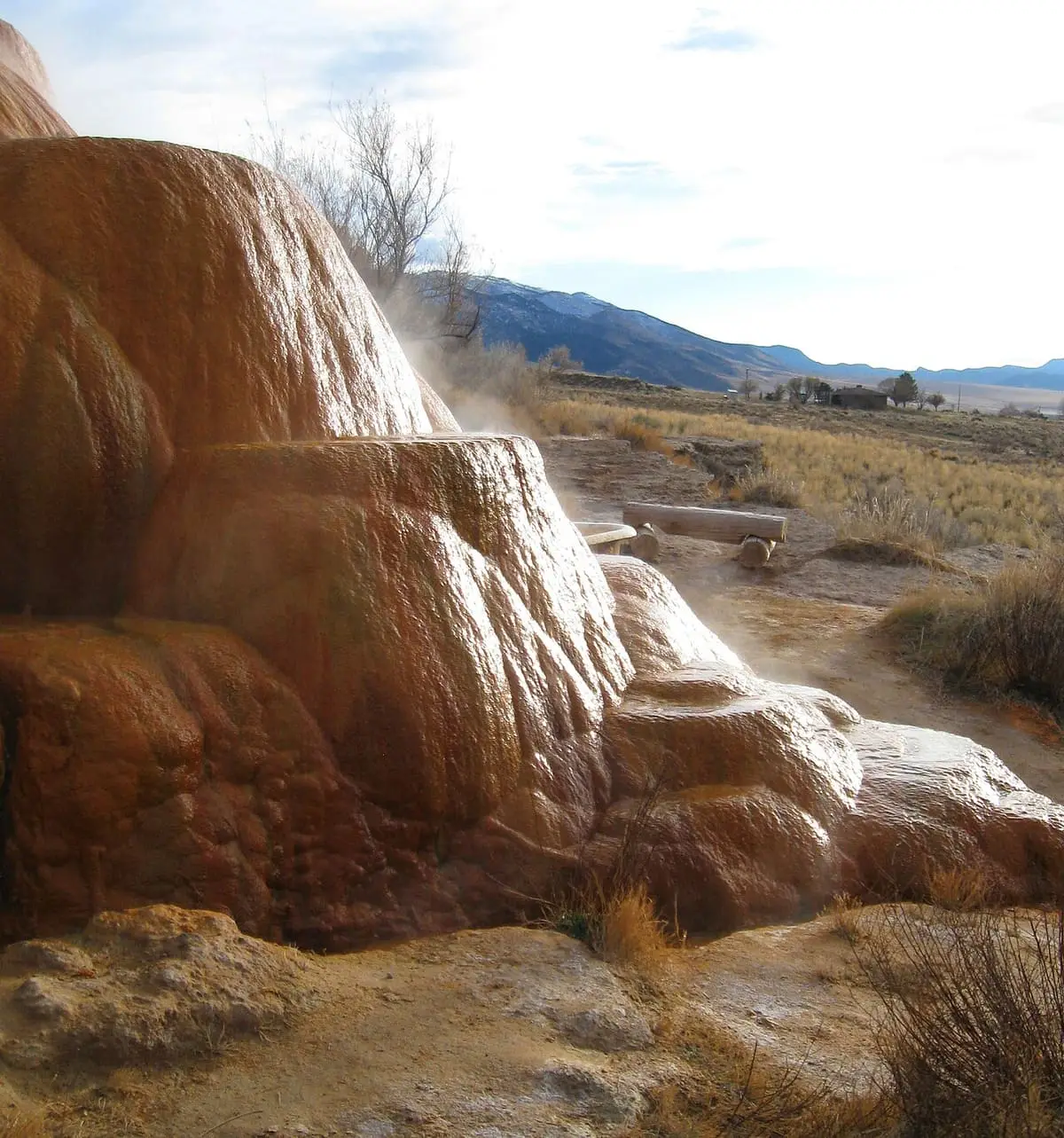 Orange and white travertine terraces of the main spring at Mystic Hot Springs above the valley